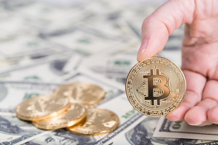 Bitcoin in female hand on dollar banknotes background, closeup