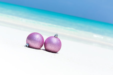 New Year decorative glitter baubles on sandy beach with sea background, Christmas Greeting card of travel vacations, copy space with crooked horizon lineの写真素材