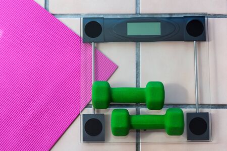 Green dumbbels on  digital glass fitness scales with pink yoga mat, Shallow DOF, top view.  Weight loss sport conceptの写真素材