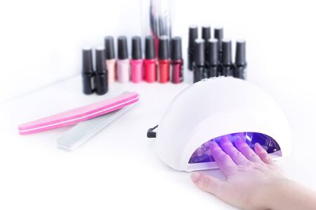 Gel nail procedure - Woman drying neils in Led Lamp on white table
の写真素材