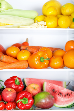 Opened refrigerator full of vegetarian healthy food, vibrant colour vegetables and fruits inside on fridgeの写真素材