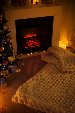 Living room with fireplace decorated for Christmas, cozy hugge interior with fir tree, gift boxes and woolen knit, super chunky yarn blanketの写真素材