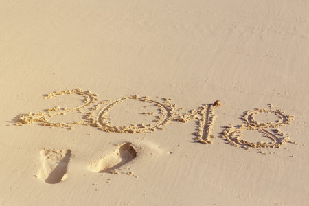Handwritting inscription numbers 2018 and footprints on perfect tropical sandy beach, travel...