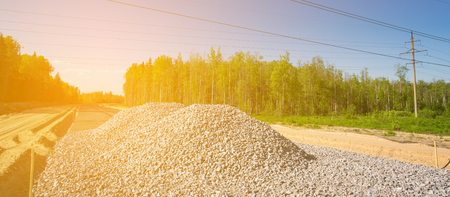 Unfinished asphalt country road in the forest. Pile of breakstones on construction siteの写真素材