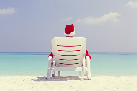 Santa Claus relaxing on chaise longue and celebrating Christmas on sandy beach, sea background with copy space. Concept of enjoy winter holidays at tropical destinationの写真素材