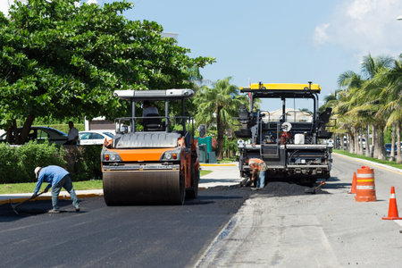 Road construction works with steamroller machine and asphalt finisher