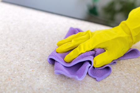 Woman's hands cleaning granite kitchen top in rubber gloves, housekeeping concept