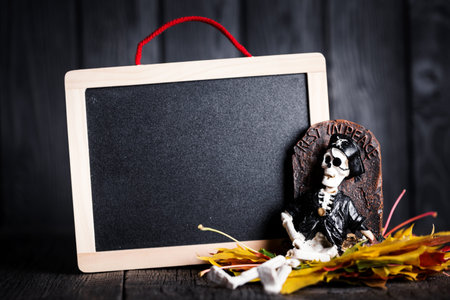 Halloween toy of skeleton with grave and chalkboard on wooden background, nobody