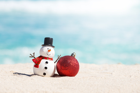 Snowman toy and christmas decoration ball at sandy beach on Caribbean sea background. New Year celebrationの写真素材