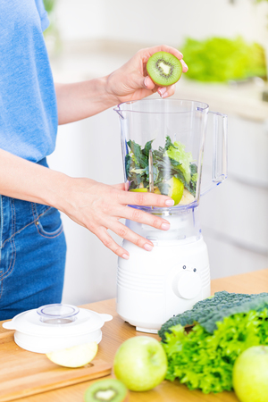 Young caucasian blond woman preparing detox fruits smoothie in blender on white kitchen, healthy eating, cooking, vegetarian food, dieting conceptの写真素材