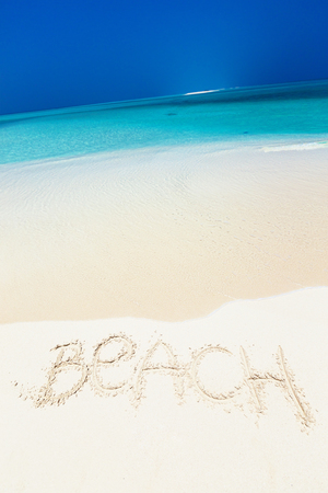Handwritting inscription word BEACH on perfect tropical sandy beach, travel concept card for vacations. Copy space with crooked horizon lineの写真素材