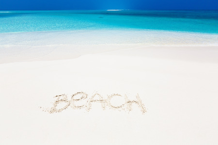 Handwritting inscription word BEACH on perfect tropical sandy beach, travel concept card for vacationsの写真素材