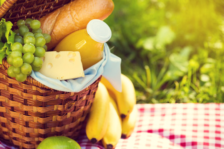 Wicker picnic basket with healthy food on red checkered table cloth on green grass outside in summer park, no peopleの写真素材