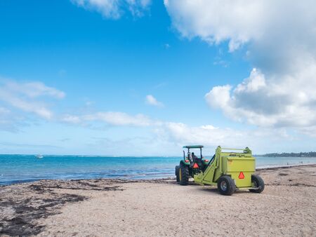 BAVARO, PUNTA CANA, DOMINICAN REPUBLIC - 24 JANUARY 2019: Cleaning sargassum algae on tropical coastline by tractor with Barber Surf Rake. Caribbean ecology problem. The Barber Surf Rake is the most popular tractor-towed beach cleaner in the worldのeditorial素材