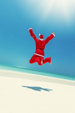 Santa Claus celebrate Christmas on sandy beach, funny jump and enjoy winter holidays at tropical destination. Greeting card for New Year travel vacations.の写真素材