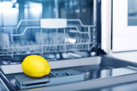 Empty dishwasher with fresh yellow lemon on shelf, aroma freshness care concept, clean equipment,  home appliance dishwashing machine in kitchen interior, no peopleの写真素材