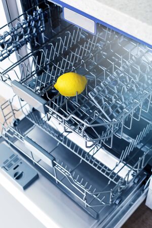 Empty dishwasher with fresh yellow lemon on shelf, aroma freshness care concept, clean equipment,  home appliance dishwashing machine in kitchen interior, no peopleの写真素材