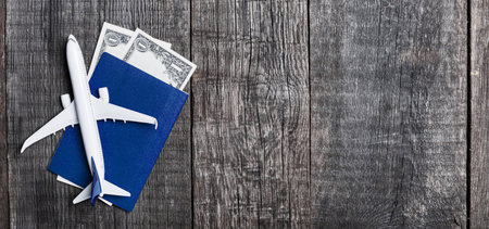 Model of airplane on passport with dollars over rustic wooden background. Top view