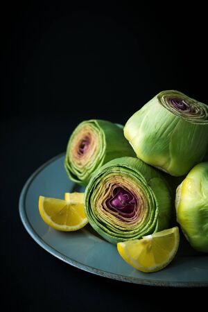 Group of fresh cleaned cut artichokes with lemon slices on grey plate, dark mood imageの写真素材