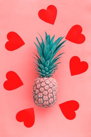 Whole pineapple tropical fruit in love with red hearts on pink pastel background, summer concept, flat lay. Romantic greeting card for vegetariansの写真素材