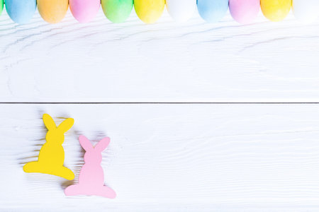 Empty rustic wooden white background, decorated rabbit and colorful pastel easter eggs. Top view...