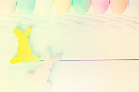 Colorful pastel easter eggs on rustic wooden white background, decorated rabbits, top view. Happy...