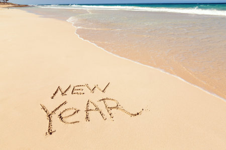 Word NEW YEAR written on sand close to sea waves. Travel, tourism and Christmas vacation concept....