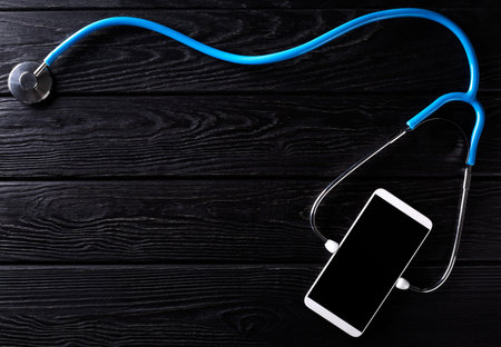 Smartphone and stethoscope on wooden rustic background. Top view. Nobody