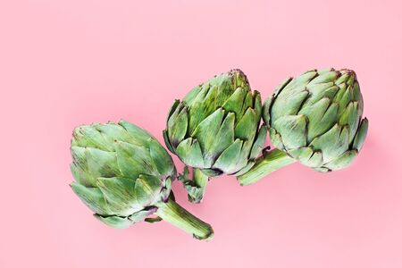 Green uncooked artichokes on pink color background, food creative conceptの写真素材