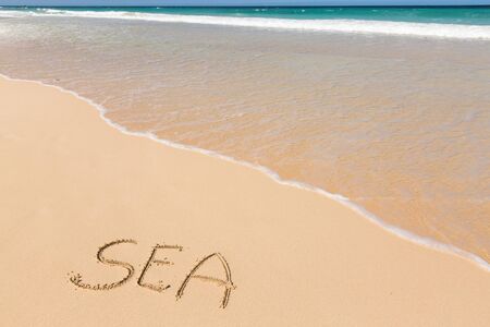 Word SEA written on sand close to sea waves. Travel, tourism, vacation concept background.の写真素材