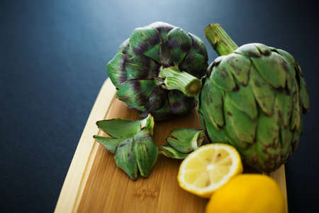 Fresh artichokes on wooden cutting board with lemons, cooking process, nobodyの写真素材