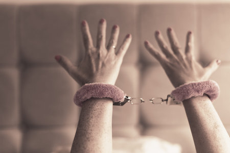 Pink sexy fluffy handcuff locked on female wrists, closeup. Erotic sex game with sexual bdsm toy in...