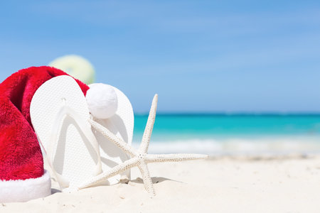 Star fish with Santa claus hat on sandy beach close to sea. Tourism and christmas vacation concept background