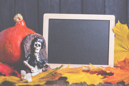 Halloween toy of skeleton with grave and chalkboard on wooden background, nobody