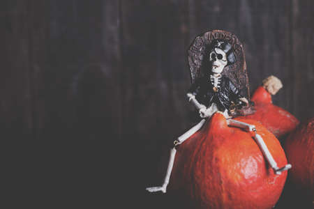Toy of skeleton with grave sitting on pumpkin over wooden background. Halloween celebrationの写真素材
