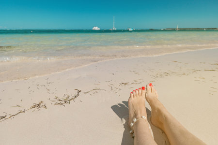 Closeup of female tanned legs on sandy dominican beach with sea view backgrouns with copy space....