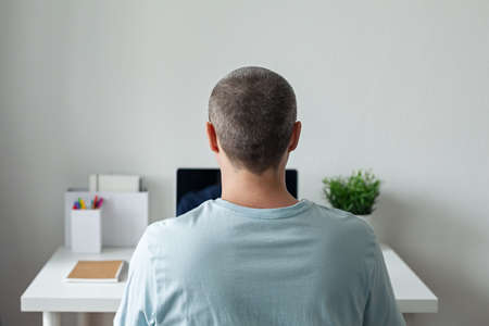 Freelancer working at home office, man using laptop at workplace inside his apartment, Back view and no face, remote work and pandemic isolation conceptの写真素材