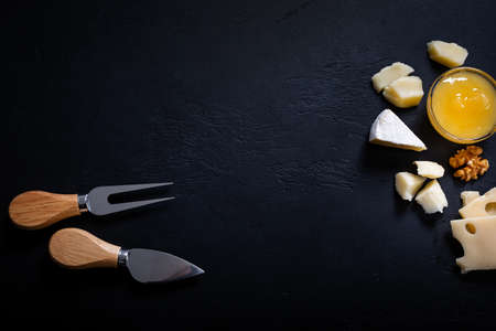 Frame of different types of cheese, fork and knife on black background. Top viewの写真素材