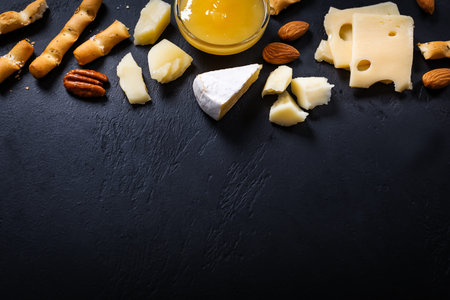 Frame of different types of cheese, fork and knife on black background. Top view, copy space for...