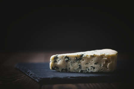 Piece of blue cheese on slate plate on dark wooden background, copy spaceの写真素材