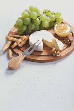 Sliced Camembert with fork on wooden cheese platter with honey and crackers on white background,