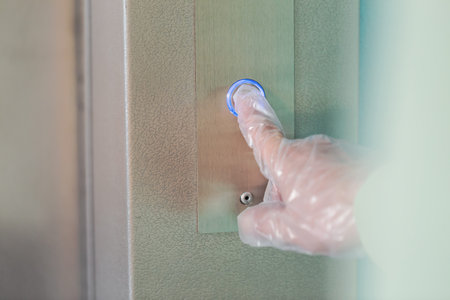 Hand in a transparent glove presses the elevator or lift button. Personal protection against...