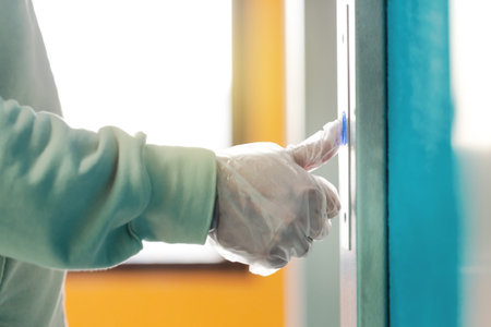 Hand in a transparent glove presses the elevator or lift button. Personal protection against...