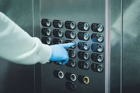 Hand in a rubber glove presses the elevator or lift button. Personal protection against bacteria and viruses. Wearing hand protective gloves in public places during Coronavirus pandemic.の写真素材