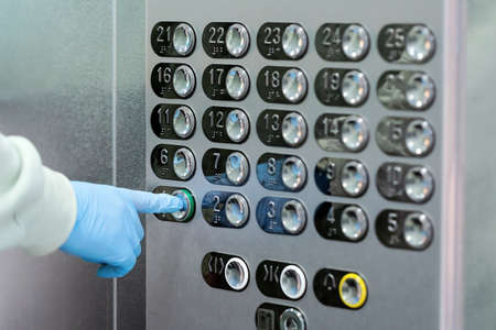 Hand in a rubber glove presses the elevator or lift button. Personal protection against bacteria and viruses. Wearing hand protective gloves in public places during Coronavirus pandemic.の写真素材