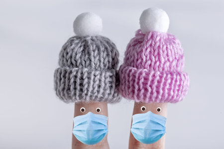Fingers in color knitted warm small hats and medical masks. Covid 19 quarantine