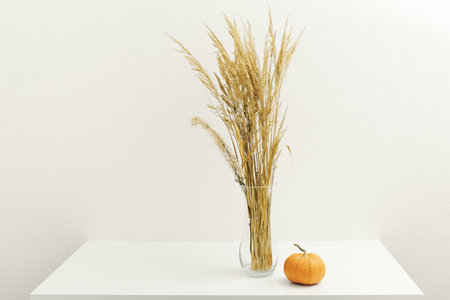 Thanksgiving Day minimal decoration. Dried beige reeds branch in vase on light beige wall background. Still life home fall decor concept with pants and pumpkinの写真素材