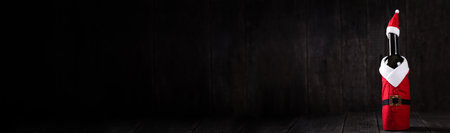 Wine bottle in Santa Claus Hat and Costume on wooden rustic background. Christmas and New Year celebration. Winter holidays. Long bannerの写真素材