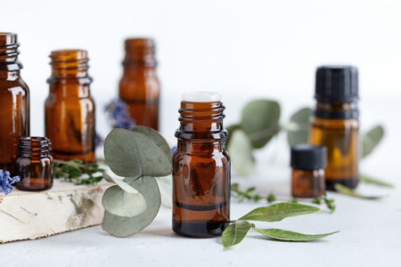 Collection of various essential oils in amber bottles with different herbal ingredients - mint, rosemary and eucalyptus leaves on neutral backgroundの写真素材
