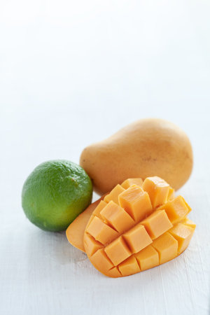 Whole fresh green lime and dice chopped yellow mango on white. Tropical fruits for immune system closeupの写真素材